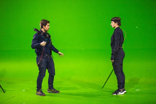 a girl and a boy standing facing each other in motion capture suits surrounded by green screens the girl is holding a fake sword and the guy is holding a camera
